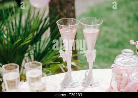 Due bicchieri di champagne rosa sul tavolo, caramelle in barattolo, garden party all'aperto, celebrazione, rosa decor. Foto Stock