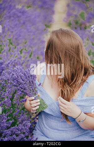 Dimensioni Plus curva donna con capelli lunghi il campo di lavanda in Surrey, Inghilterra, Mayfield . Moda abiti vestito blu, tenere premuto bouquet di fiori . Vista laterale. Foto Stock