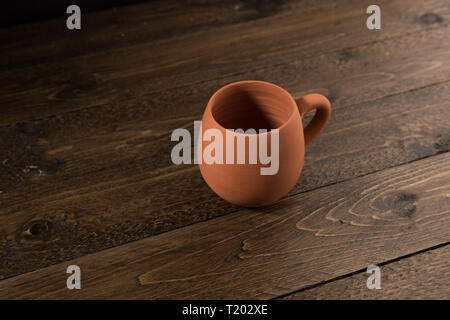 Vuoto non verniciata tazza di argilla sul tavolo di legno con sfondo nero Foto Stock