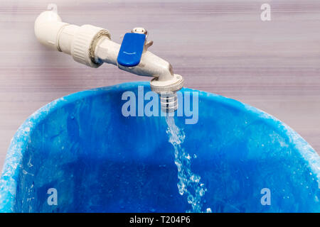 Da aprire rubinetto sporco scorre un flusso di acqua in un secchio blu Foto Stock