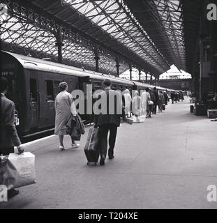 1960s, Victoria Station, Londra, passeggeri con bagagli che camminano lungo il binario o l'atrio dopo essere sbarcati dal treno. Foto Stock