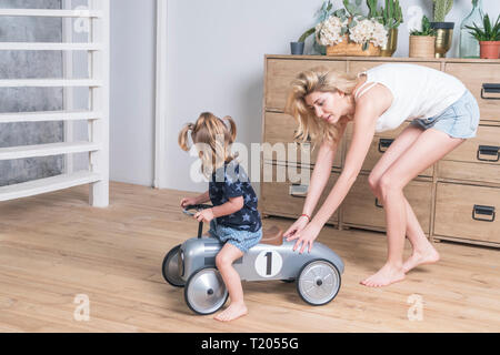 Rotoli di madre la figlia su una macchina giocattolo in camera vicino la cassettiera Foto Stock