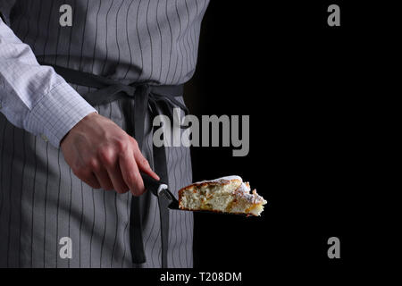 Lo chef tenendo in mano un pezzo di torta su sfondo nero. rendendo torta e servire. Foto Stock