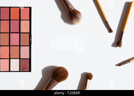 Vista superiore del make up cosmetici e accessori. Ombretto tavolozza e pennelli naturali con impugnature in legno. Sfondo bianco. Foto Stock