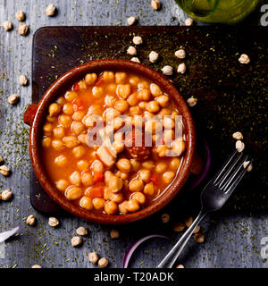 Angolo di alta vista di una casseruola di terracotta con garbanzos a la riojana, uno spagnolo spezzatino di ceci, su un tagliere di legno posto su un rustico woode Foto Stock