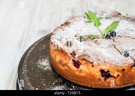 Torta fatta in casa con ribes nero, spolverati con zucchero a velo e vive la menta su uno sfondo scuro panificio concetto. Foto Stock