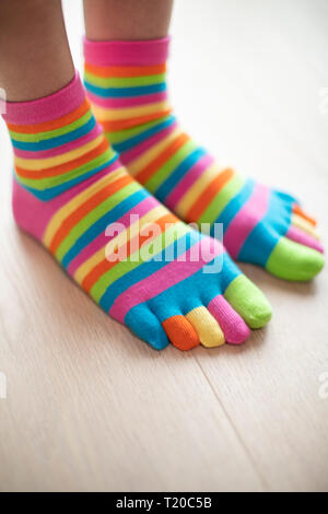 Close up della donna che indossa vivacemente colorato calze su piedi in piedi sul pavimento in legno Foto Stock