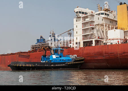 Operazioni portuali per la gestione e il trasporto di minerali di ferro.Tirare la manovra e girando il trasbordo nave prima di docking e di carico di minerale fino al molo Foto Stock