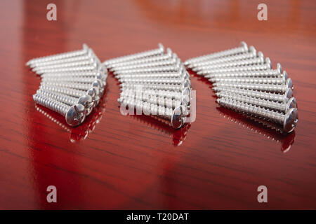 Tre gruppi di viti argento disposti in fila su una superficie con finitura in legno Foto Stock