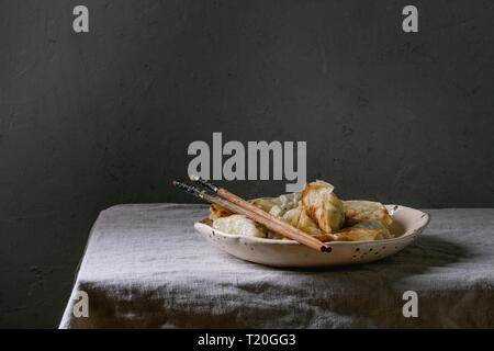 Fritti gnocchi asiatici Gyozas potstickers in bianco piastra ceramica servita con bacchette sulla tabella di lino inumidito. Cena asiatica Foto Stock