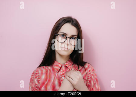 Close up ritratto di giovane donna con tiene le mani sul cuore, vestito in maglietta rossa, esprime gratitudine, ha friendly espressione facciale, isolate su p Foto Stock