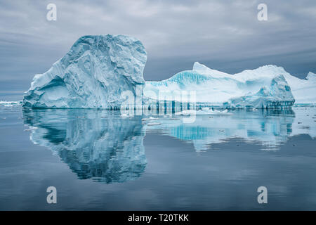 Un incredibile iceberg nel cimitero di ghiaccio in Antartide che provoca una bella riflessione sulla superficie dell'acqua, mentre in uno zodiaco Foto Stock