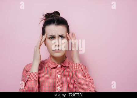 Giovani stanchi brunette donna indossa maglietta rossa, mantiene il dito su templi, soffre di mal di testa, si sente dolore, essendo oberati di lavoro, bisogno di riposo e tranquillità. Persone, Foto Stock