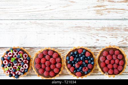Lampone e mirtillo pasticcini con glassa al cioccolato, fresco di bacche e foglie di menta, il fuoco selettivo. Frutta fresca tart su sfondo bianco, freschi Foto Stock