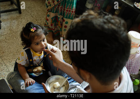 Un indiano Bengali bella ragazza neonato Bambino è avente le caramelle dalla sua mano del padre dentro la sua stanza. Foto Stock