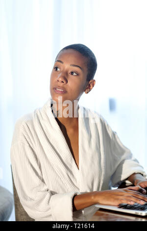 Un Afro donna latinoamericana con strettamente tagliato i capelli lavorando a un computer portatile accanto a una finestra Foto Stock