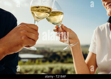 Chiudere fino alle mani di un paio di occhiali di tostatura di vino bianco seduti all'aperto. Tagliate il colpo di un paio di vino di tostatura. Foto Stock