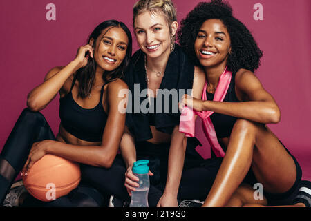 Diversi gruppi di donne fitness seduti insieme in studio e guardando la telecamera sorridendo. Gruppo di femmine riposo dopo esercizio. Foto Stock