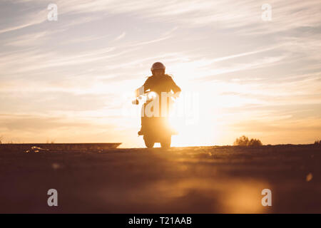 Silhouette di uomo che cavalca custum motocicletta al tramonto Foto Stock