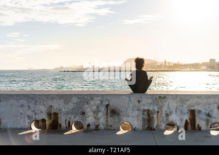 Spagna, Barcellona, vista posteriore della donna seduta sulla parete di fronte al mare in meditazione Foto Stock