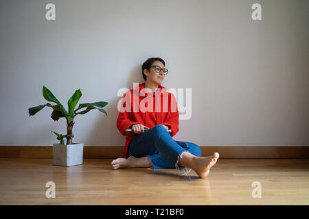 Giovane donna seduta sul pavimento, fantasticando Foto Stock