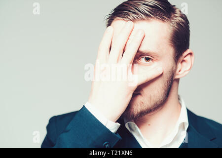 Modello bionda isolato su sfondo grigio. Barbuto ragazzo con gli occhi di nocciola che copre la sua faccia con palm Foto Stock