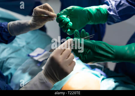 I chirurghi azienda bisturi chirurgico e forcipi in sala operatoria durante un intervento chirurgico in ospedale Foto Stock