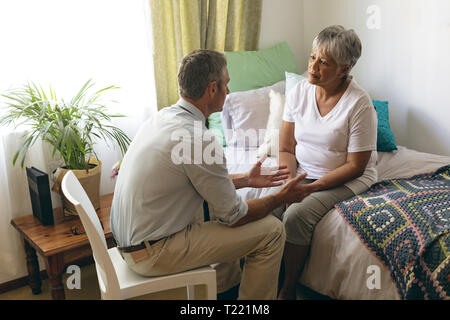 Medico maschio interagenti con il senior paziente di sesso femminile al momento del pensionamento home Foto Stock