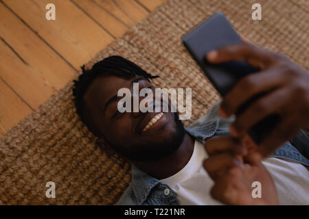 Uomo bello usando il cellulare mentre giacente sul piano a casa Foto Stock