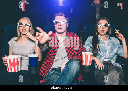 Stupiti e sorpresi gli adolescenti sono la visione di film in 3d. Essi indossare occhiali per l. Ragazzo sta cercando di raggiungere lo schermo con la sua mano. Le ragazze sono seduta b Foto Stock