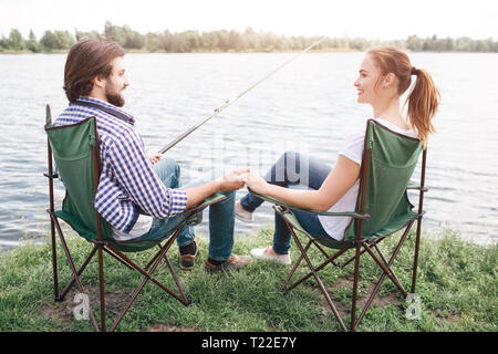 Coppia adorabile è seduta in morbide sedie vicino alla riva del fiume e guardando ogni altro. Il ragazzo è tenendo la mano della bambina. e tenendo un pesce-biella con l'altra. Foto Stock