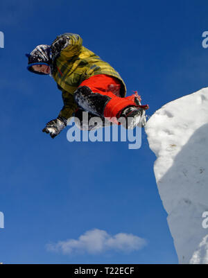 Un giovane ragazzo (6 anni) jumping dalla cima di una scogliera di neve Foto Stock