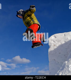 Un giovane ragazzo (6 anni) jumping dalla cima di una scogliera di neve Foto Stock