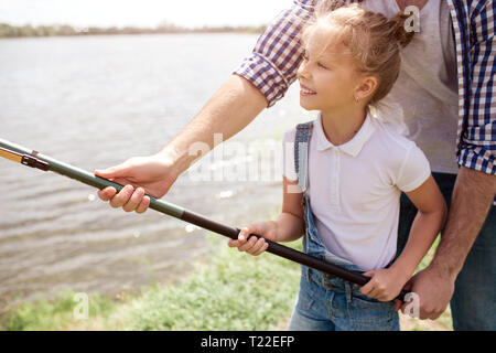 Una foto di guy aiutando la figlia per tenere il pesce-asta in un modo giusto. La ragazza è presa con entrambe le mani e sorridente. Lei sembra felice Foto Stock