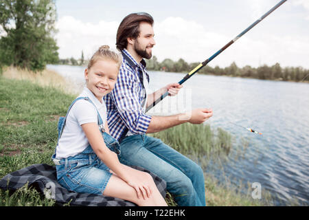 La ragazza è seduta oltre a suo padre e a guardare la fotocamera. Il ragazzo è azienda gish-asta e pesca. Egli è concentrata sulla pesca. Il clima è molto beau Foto Stock