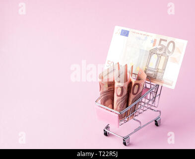 Carrello per supermercati piena di banconote in euro su un sfondo rosa con copia spazio. Il libero commercio. mercato monetario. Stile minimalista. Shop Carrello al supermercato. Foto Stock