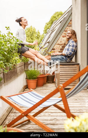 Coppia giovane seduto sul proprio balcone in estate, parlando e utilizzando computer portatile Foto Stock