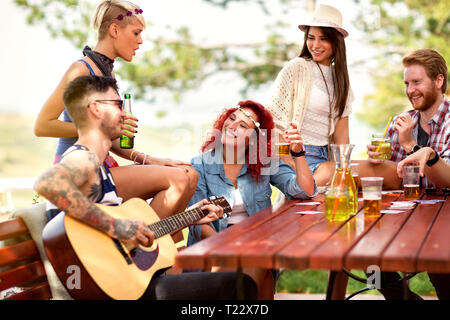 Vivace ragazza di zenzero toast con tatuato maschio di amici che suona la chitarra nel ristorante in aperta Foto Stock
