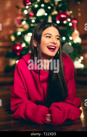 Ritratto di ridere ragazza adolescente sdraiato sul pavimento nella parte anteriore del albero di Natale Foto Stock