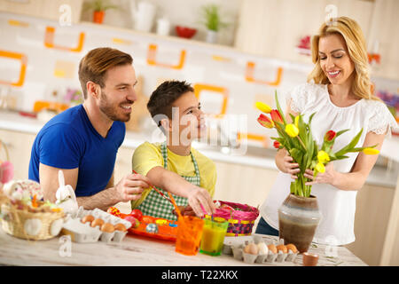 Padre con figlio colorare le uova di Pasqua mentre madre organizza i tulipani in vaso Foto Stock