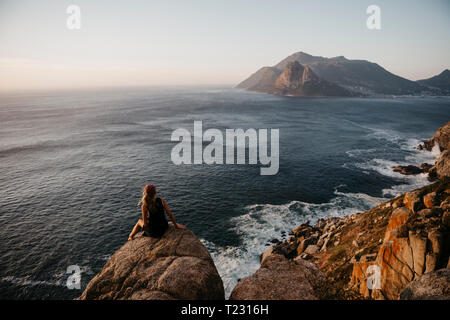 Sud Africa, Western Cape, donna seduta su una roccia a guardare vista, visto da Chapman's Peak Drive Foto Stock