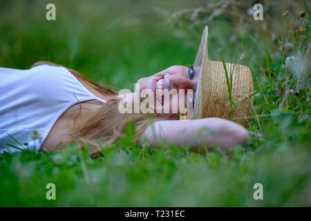 Ritratto di ridere ragazza adolescente indossando cappello di paglia sdraiati su un prato in estate Foto Stock
