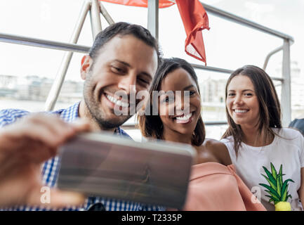 UK, Londra, happy amici prendendo un selfie durante un viaggio in barca sul fiume Tamigi Foto Stock