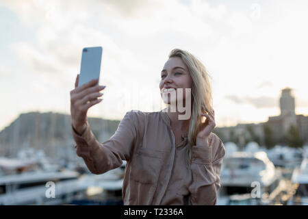 Sorridente giovane donna prendendo un selfie al waterfront Foto Stock