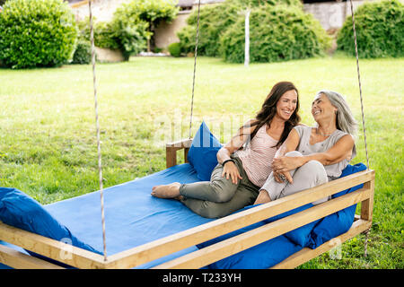 Due felici donne rilassante su un letto sospeso in giardino Foto Stock