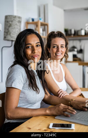 Ritratto di due donne sorridente seduto con il computer portatile a tavola in casa Foto Stock