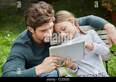 Padre e figlia utilizzando tablet insieme in giardino Foto Stock