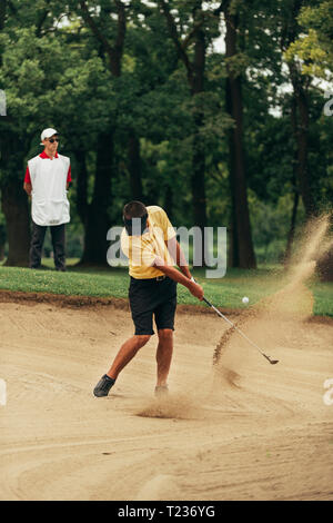 Il Golfer giocando da bunker, caddy dietro. Foto Stock