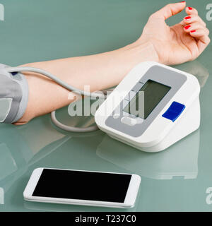 La misura della pressione del sangue in casa, utilizzando smart phone per seguire i risultati. Foto Stock