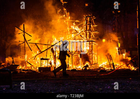 Silhouette di un vigile del fuoco cercando di controllare un incendio in una strada nel corso di una notte. Foto Stock